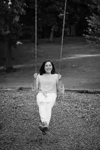 Black and White fun girl senior photo on swing in park.