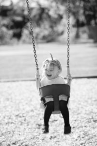 Black and White photo of girl laughing on swing during photography session.