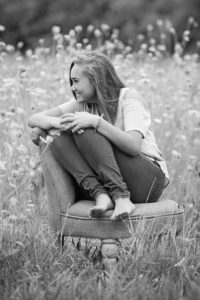 Professional black and white photo of girl smiling curled up in chair in a field.