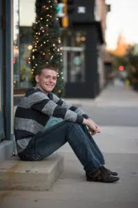 Guys smiling ini front of Christmas lights during senior photo session.